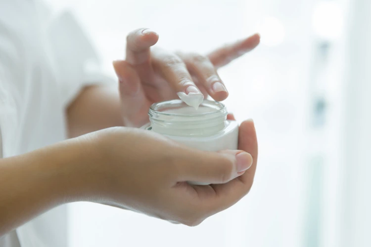 Lady holding and using a bottle of acne cream.