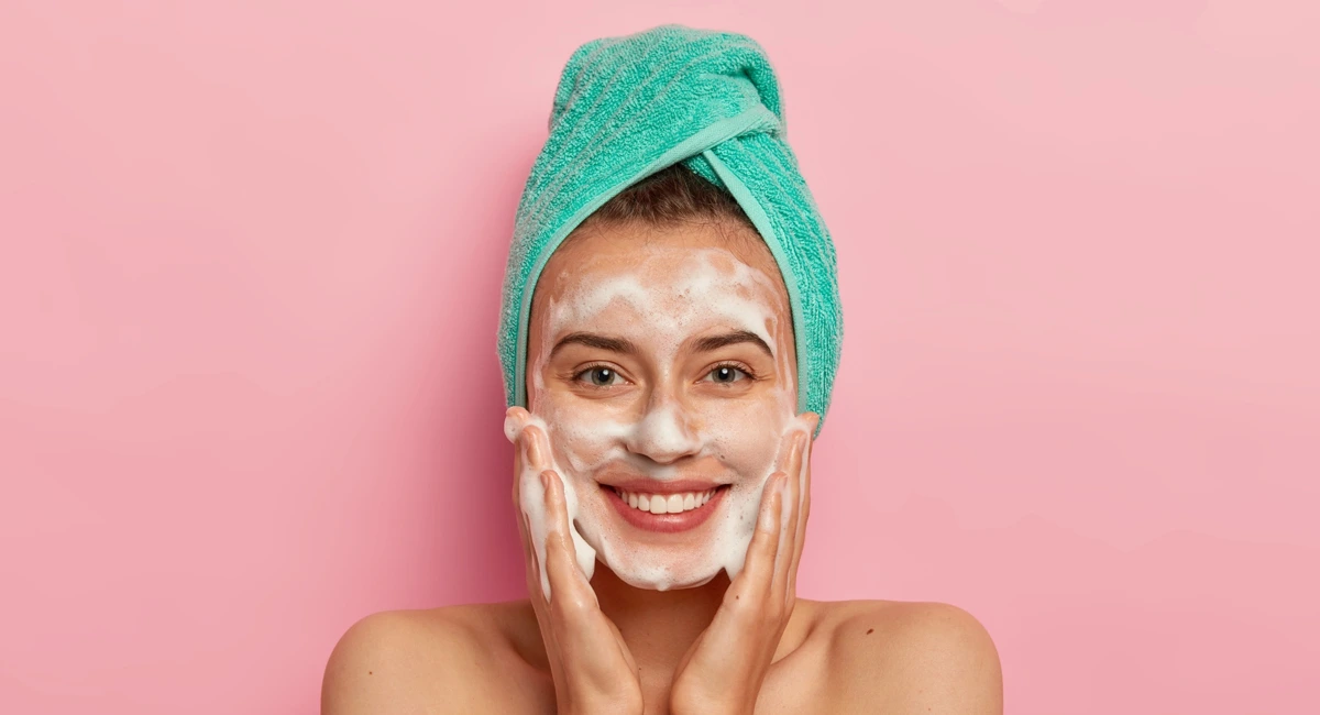 Lady with healthy complexion cleansing her face with skin care products.