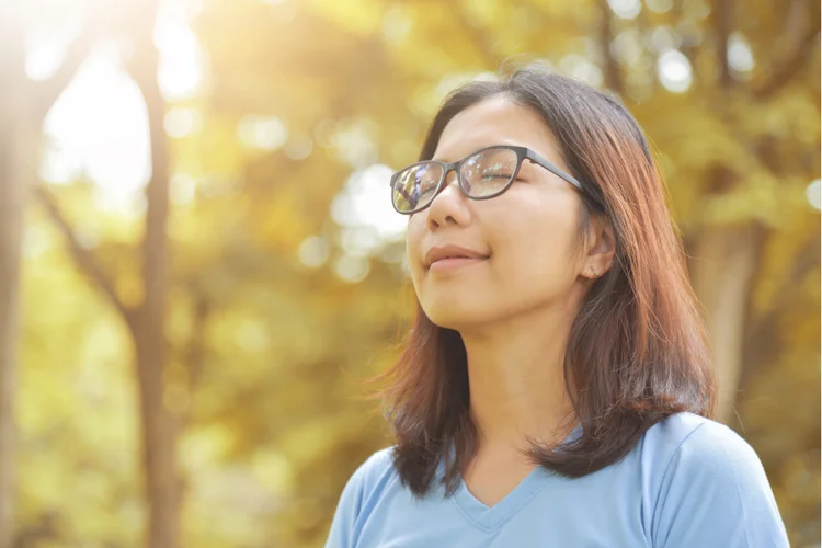 Asian female practicing mindfulness outdoors to lower stress levels, thereby improving skin health.