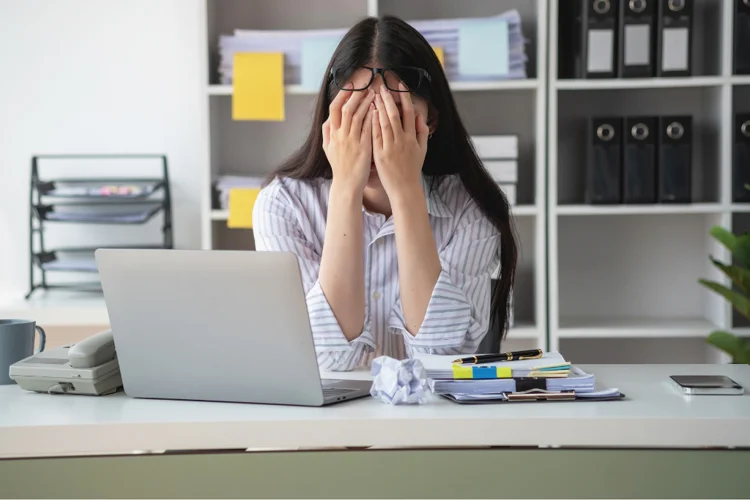 Asian woman feeling stressed at work due to tight deadlines, which can trigger stress acne.