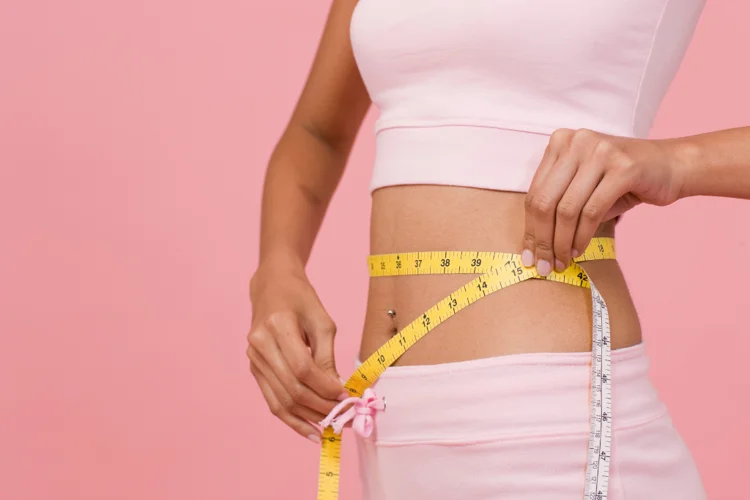 Asian woman measuring her waist after undergoing a medically supervised weight-loss programme.