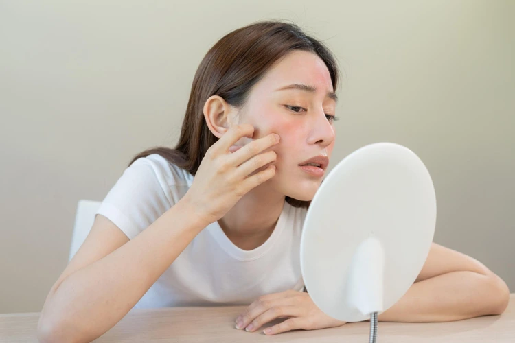 A concerned looking lady examining the acne scars on her face using a mirror.