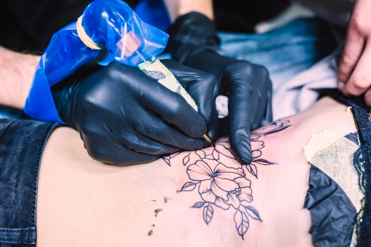 A female client getting a tattoo drawn on her back area by a tattoo artist.